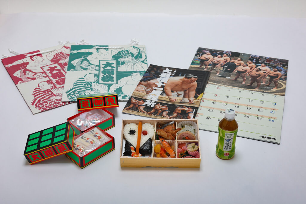 軍配幕ノ内弁当 お茶 大相撲カレンダー 九州場所パンフレット 明け荷の箱に入ったお菓子（力士柄の金太郎飴・カレー味のあられ） 相撲柄紙袋 のセットです。